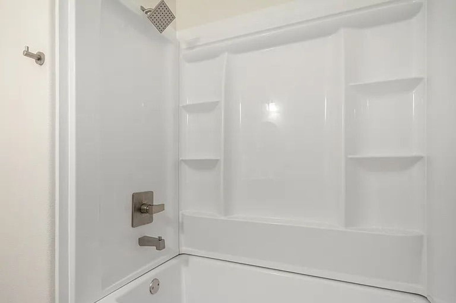 Clean white fiberglass bathtub and shower combination unit featuring built-in corner shelves and brushed nickel hardware.