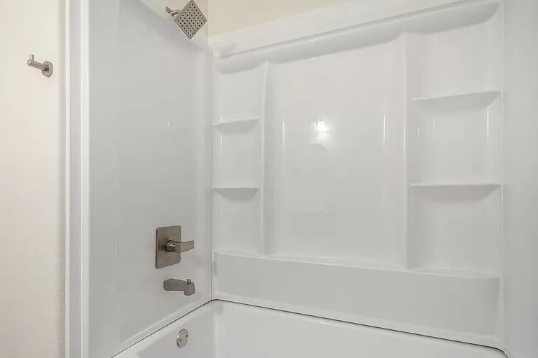 Clean white fiberglass bathtub and shower combination unit featuring built-in corner shelves and brushed nickel hardware.