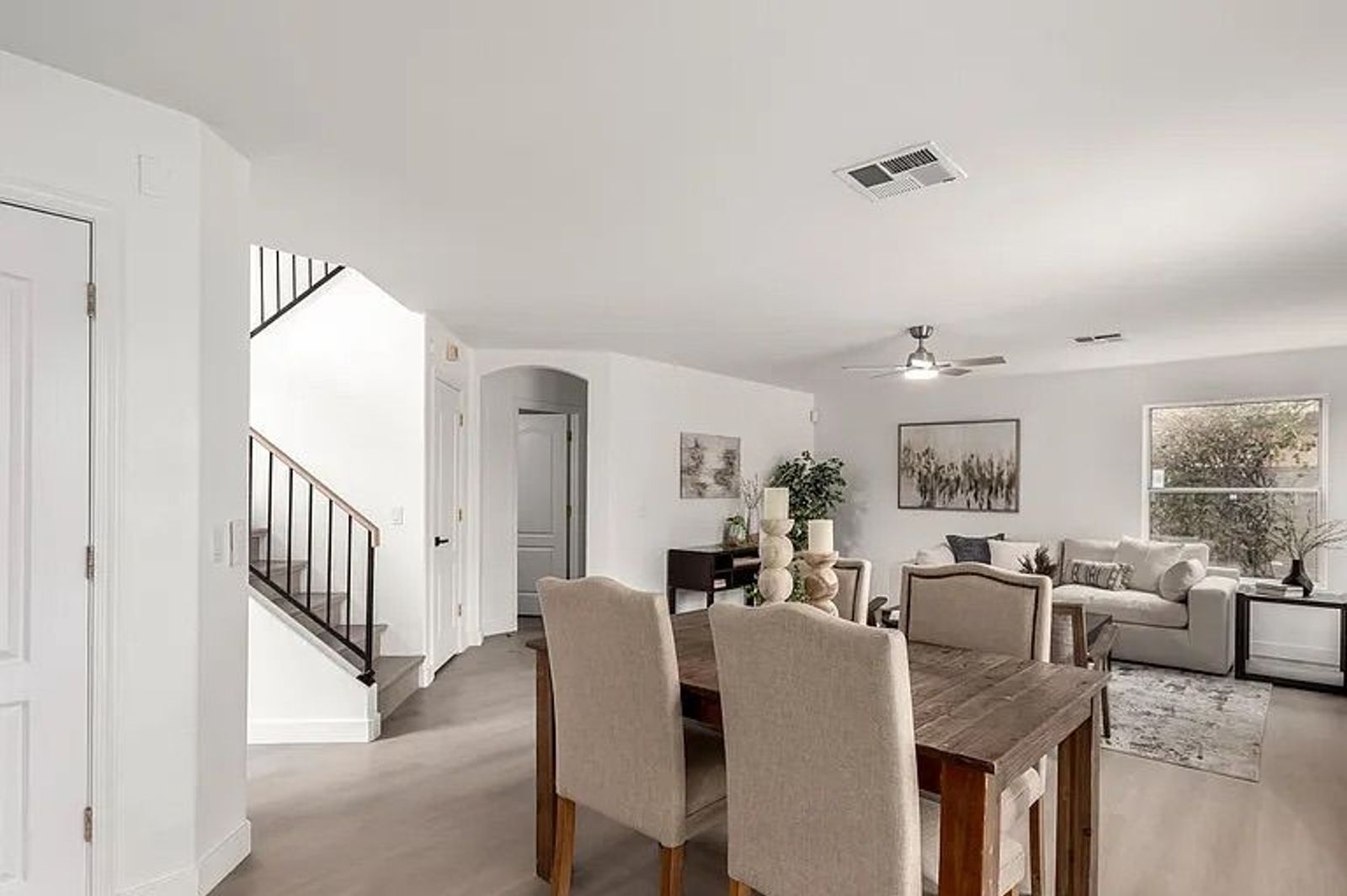 Open concept dining area featuring a rustic wood table with upholstered chairs, situated next to a staircase and adjacent living room.