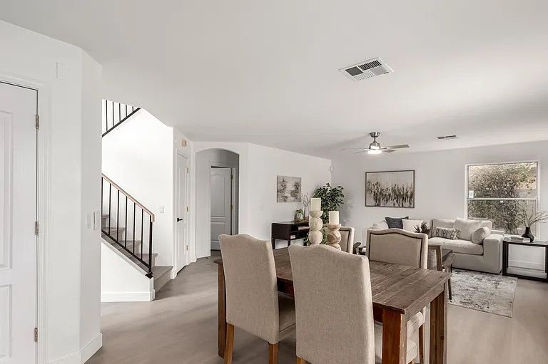 Open concept dining area featuring a rustic wood table with upholstered chairs, situated next to a staircase and adjacent living room.
