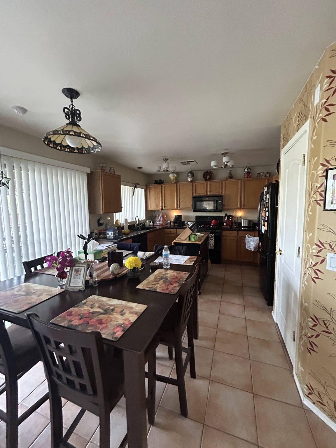 Before the remodel: the original kitchen seen from the dining table, with oak cabinets, black appliances, a tile floor and the pantry door at right.