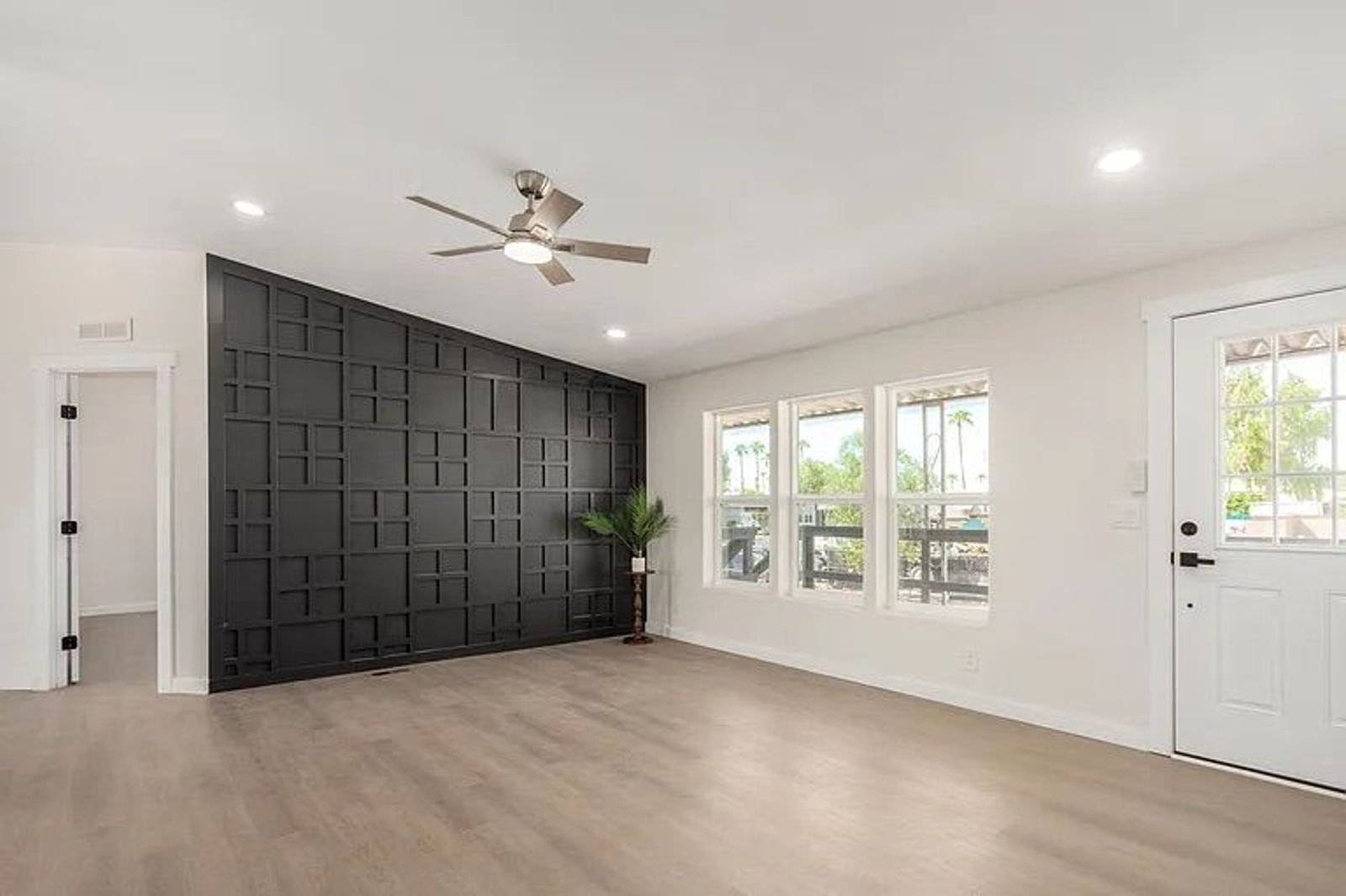 Living room entry area featuring a striking black geometric paneled accent wall, light wood-look flooring, and a white front door.
