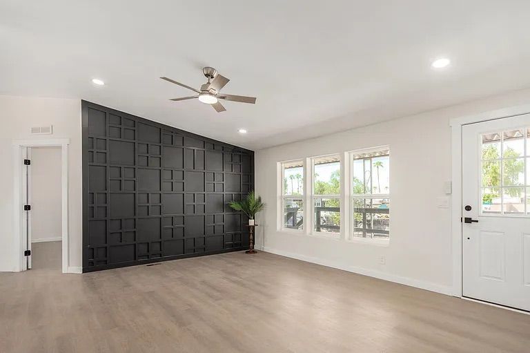 Living room entry area featuring a striking black geometric paneled accent wall, light wood-look flooring, and a white front door.