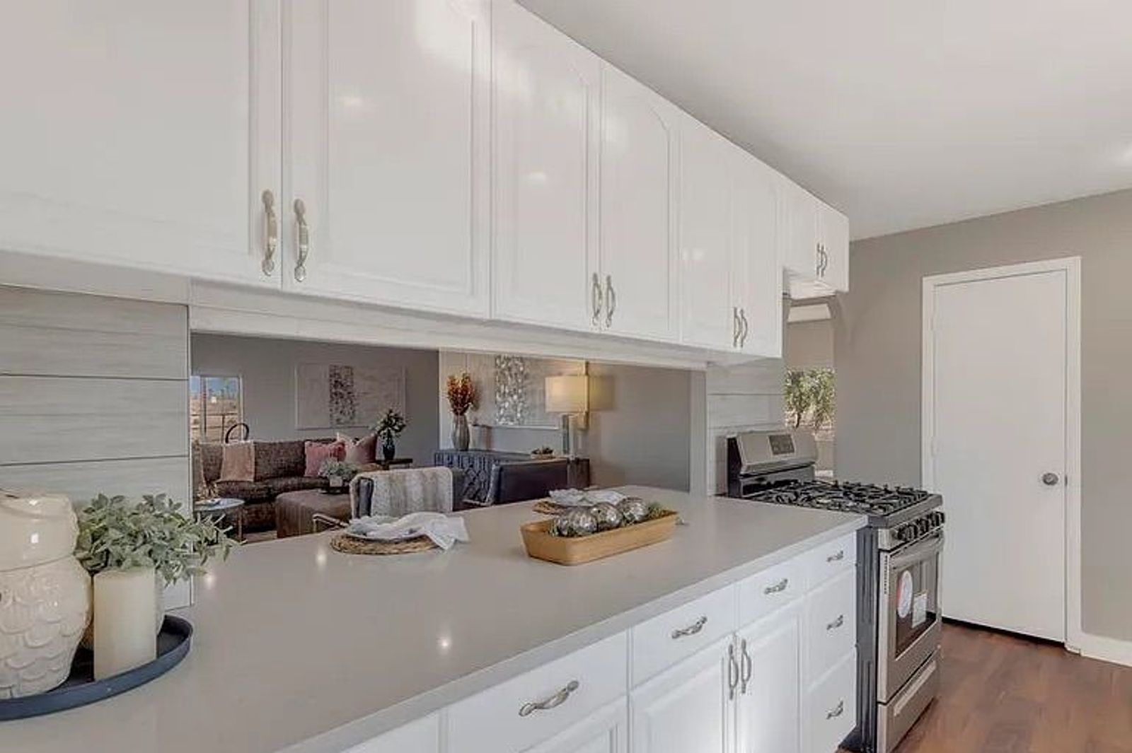 White kitchen cabinets and light grey countertops featuring a large horizontal mirror that reflects the adjacent living room area.