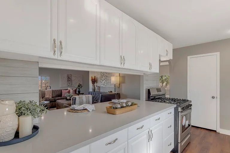 White kitchen cabinets and light grey countertops featuring a large horizontal mirror that reflects the adjacent living room area.