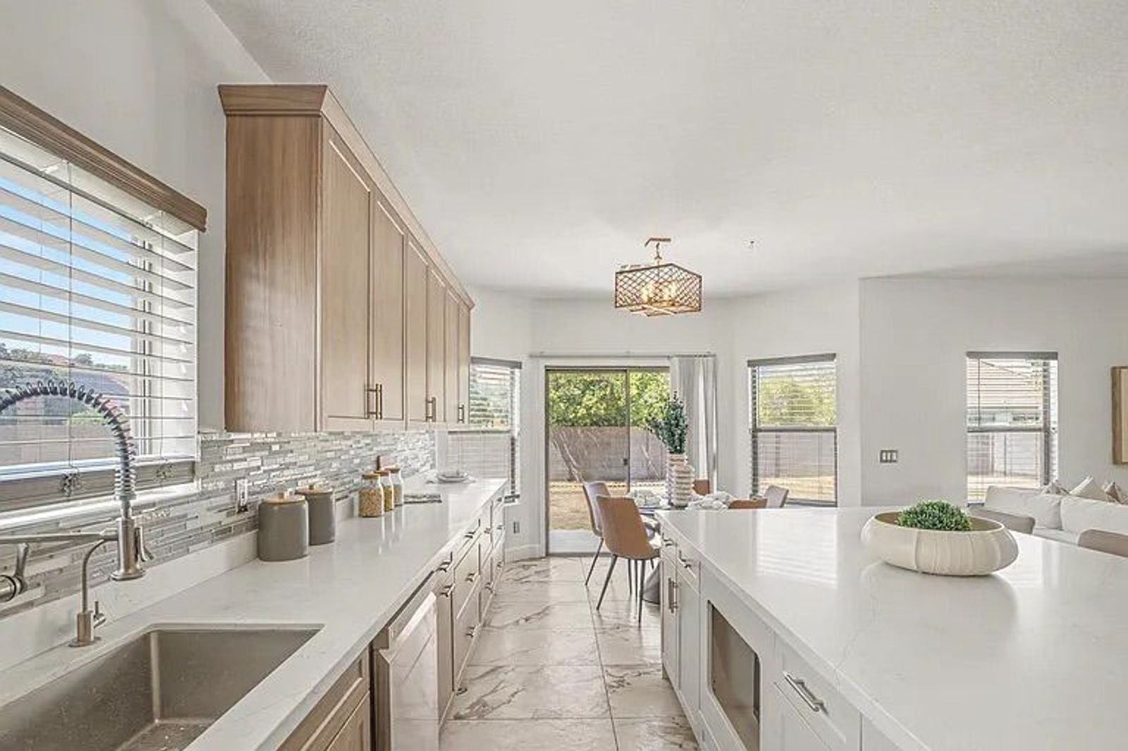 Kitchen area showing an undermount sink, white quartz countertops, wood-style cabinets, and a clear view into the adjacent dining nook and backyard.