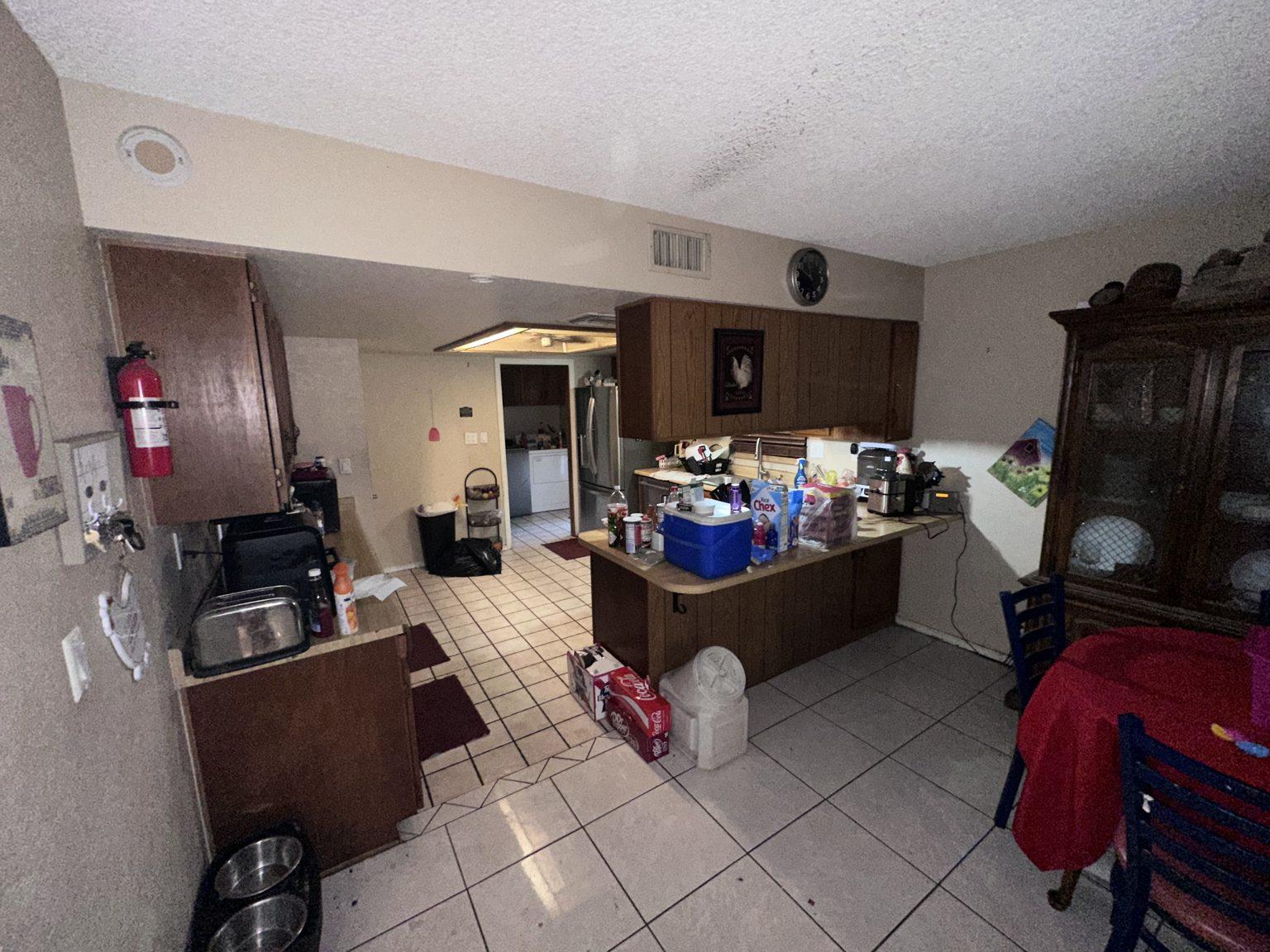 Before the remodel: the original kitchen with dark wood cabinets, a peninsula counter and white tile floor, seen from the dining area.