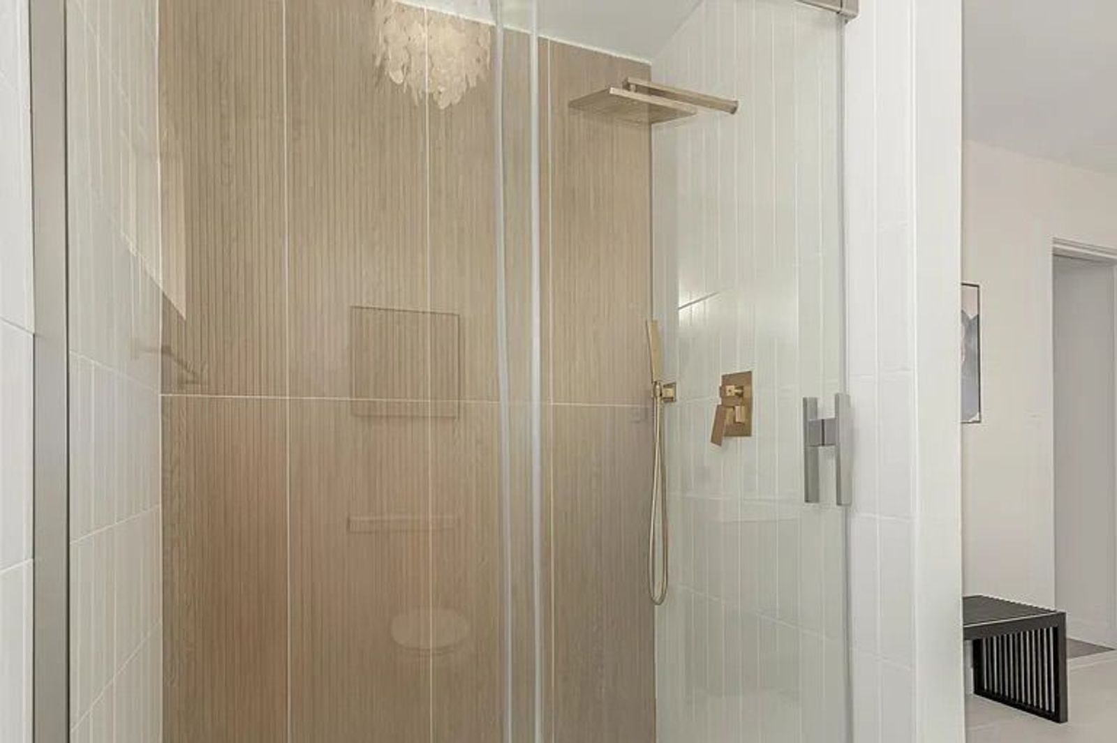 Modern glass-enclosed shower featuring a vertical wood-look accent tile wall, white tiled side walls, and brushed gold fixtures including a square rain showerhead.