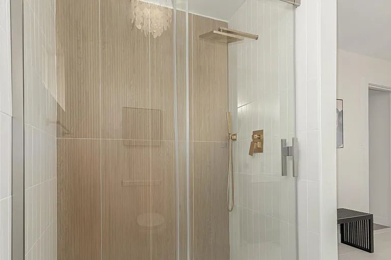 Modern glass-enclosed shower featuring a vertical wood-look accent tile wall, white tiled side walls, and brushed gold fixtures including a square rain showerhead.