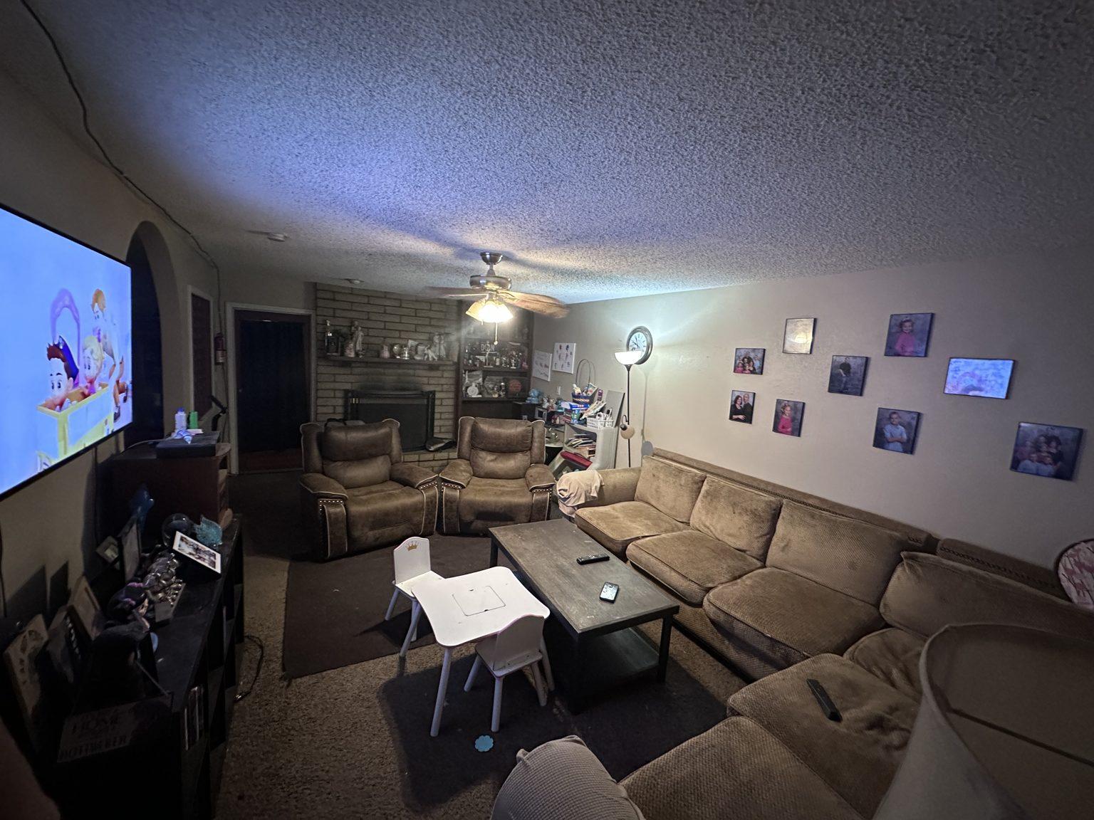 Before the remodel: the original living room with a brown sectional, brick fireplace and wall-mounted TV.