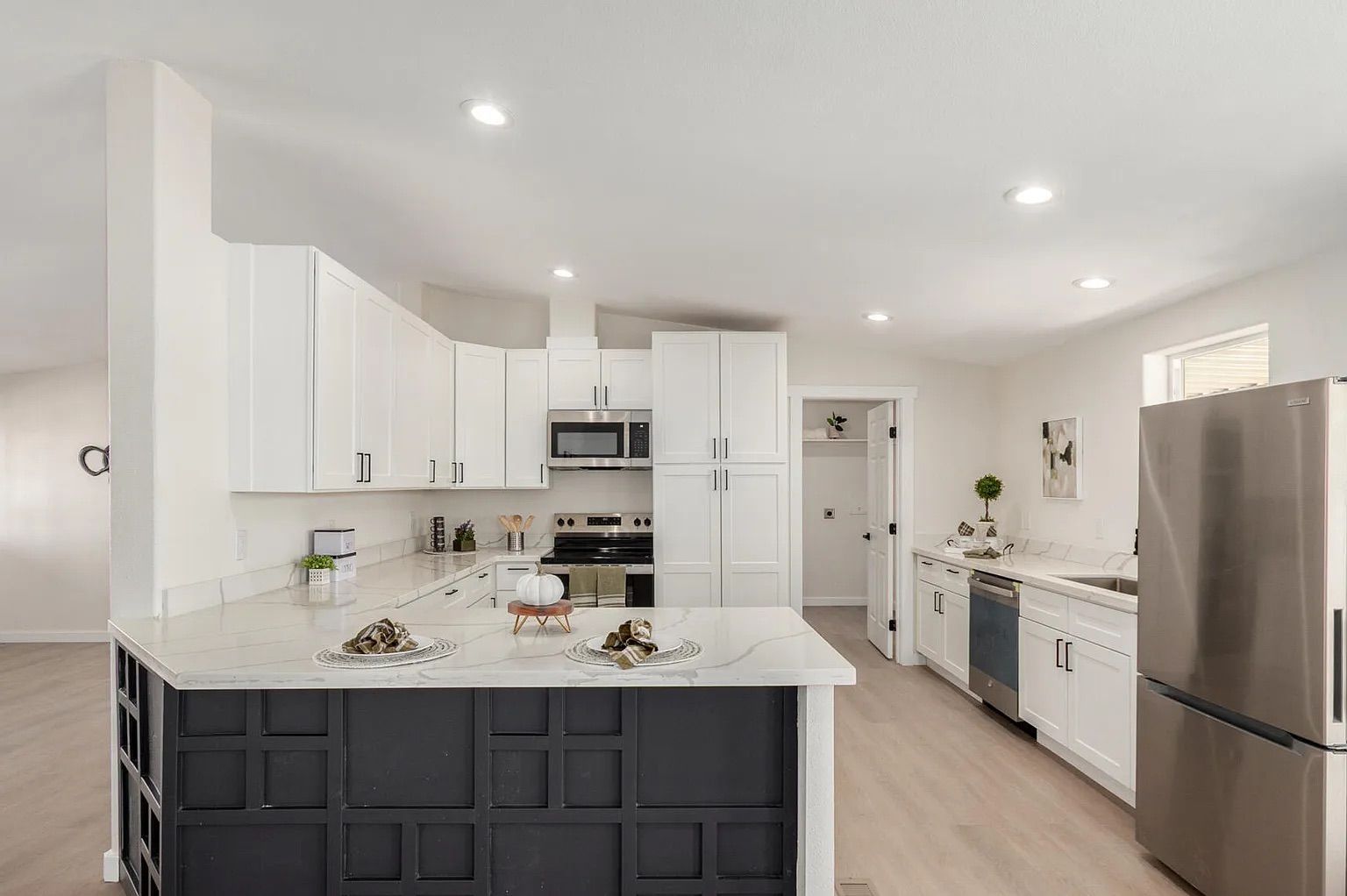 Modern kitchen featuring white shaker cabinets, marble-look countertops, stainless steel appliances, and a peninsula with a black geometric paneled base.
