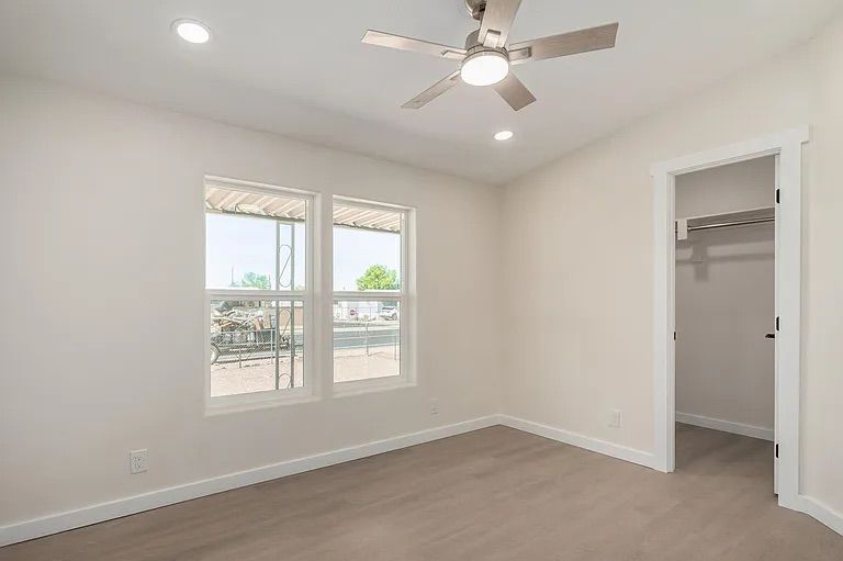 Empty bedroom featuring light wood-style flooring, a modern ceiling fan, two side-by-side windows, and an open doorway leading into a walk-in closet.