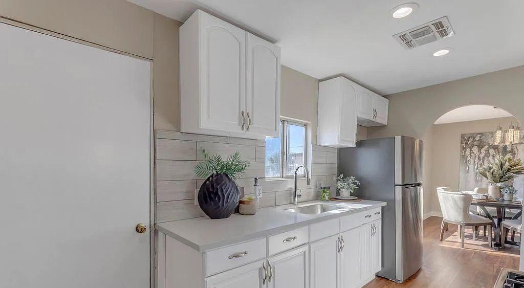 Kitchen area featuring white shaker cabinets, stainless steel appliances, a light tile backsplash, and dark wood flooring extending into the adjacent dining room.