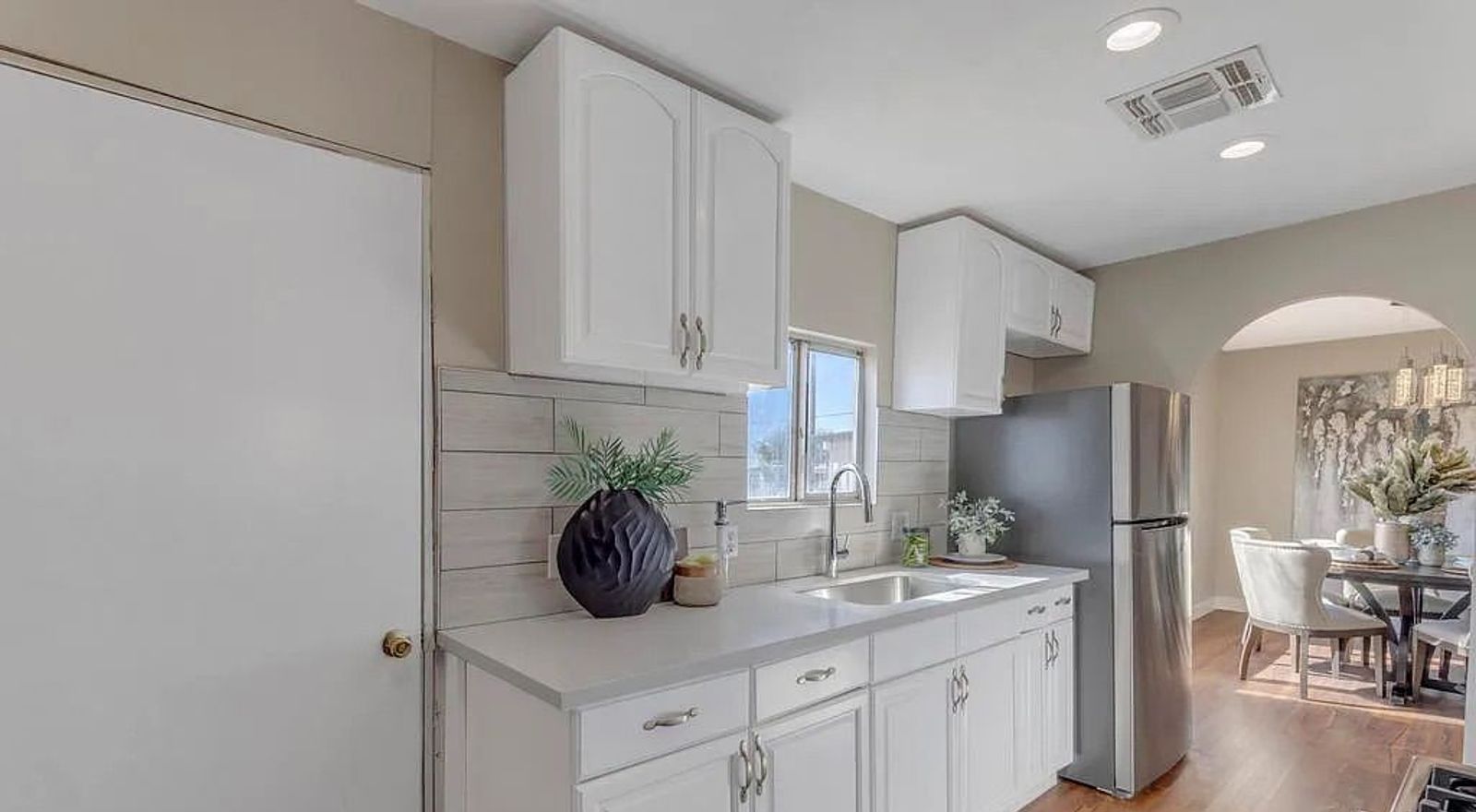 Kitchen area featuring white shaker cabinets, stainless steel appliances, a light tile backsplash, and dark wood flooring extending into the adjacent dining room.