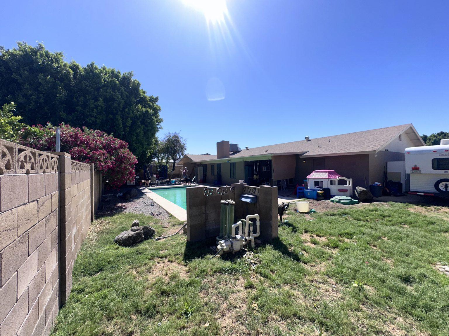 Before the remodel: the backyard seen from the far corner, with patchy grass, a block wall and the pool at right.