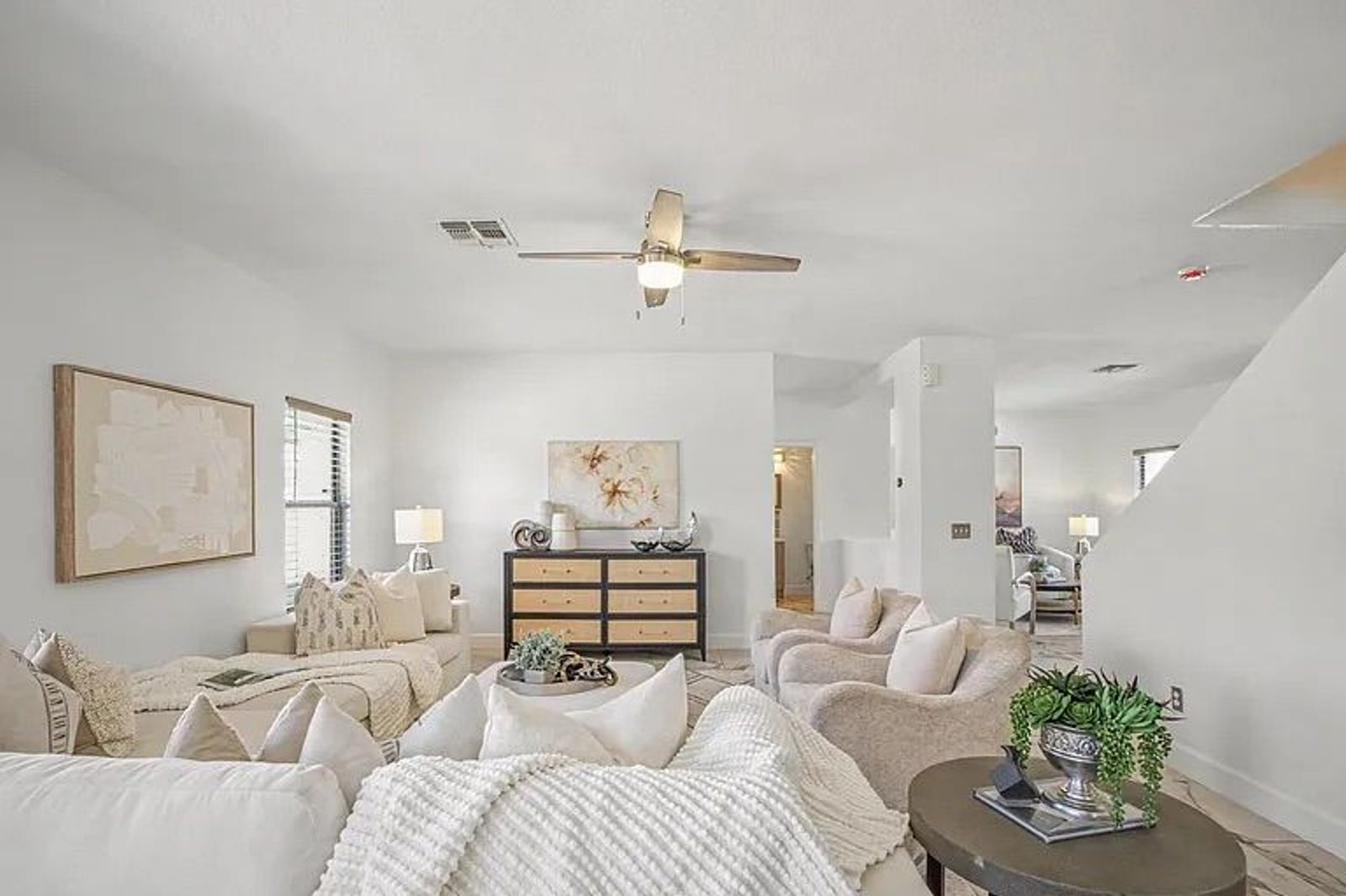 Open living room space featuring a massive white sectional sofa, layered pillows, a black and cane console table, and a view connecting to the home's staircase.
