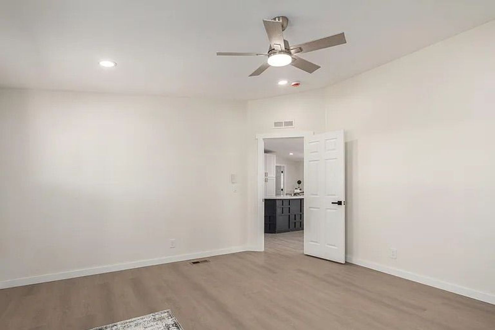 Empty room featuring light wood-style flooring, a contemporary ceiling fan, and double doors opening directly into the home's kitchen.