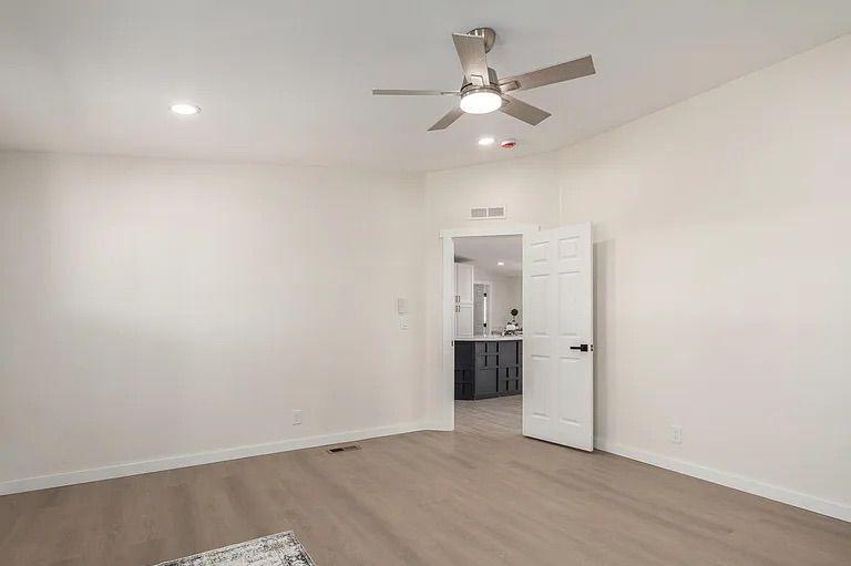 Empty room featuring light wood-style flooring, a contemporary ceiling fan, and double doors opening directly into the home's kitchen.