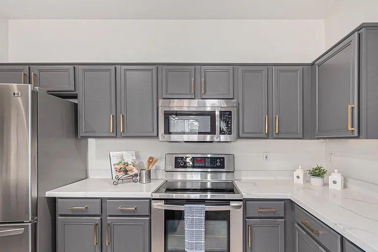 Corner view of a kitchen featuring dark grey shaker cabinets, white quartz countertops, and a stainless steel electric range and microwave.
