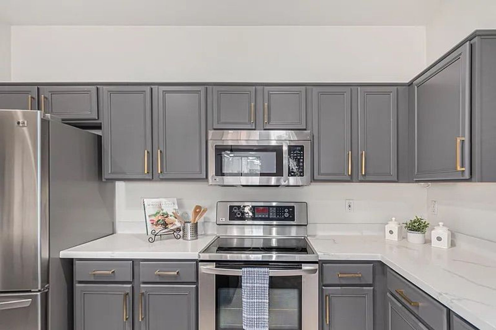 Corner view of a kitchen featuring dark grey shaker cabinets, white quartz countertops, and a stainless steel electric range and microwave.