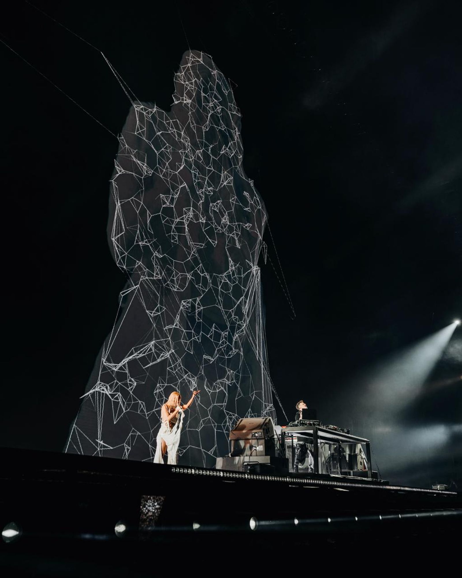Aimée Sophia on stage beneath a towering wireframe projection — the voice rendered as living architecture