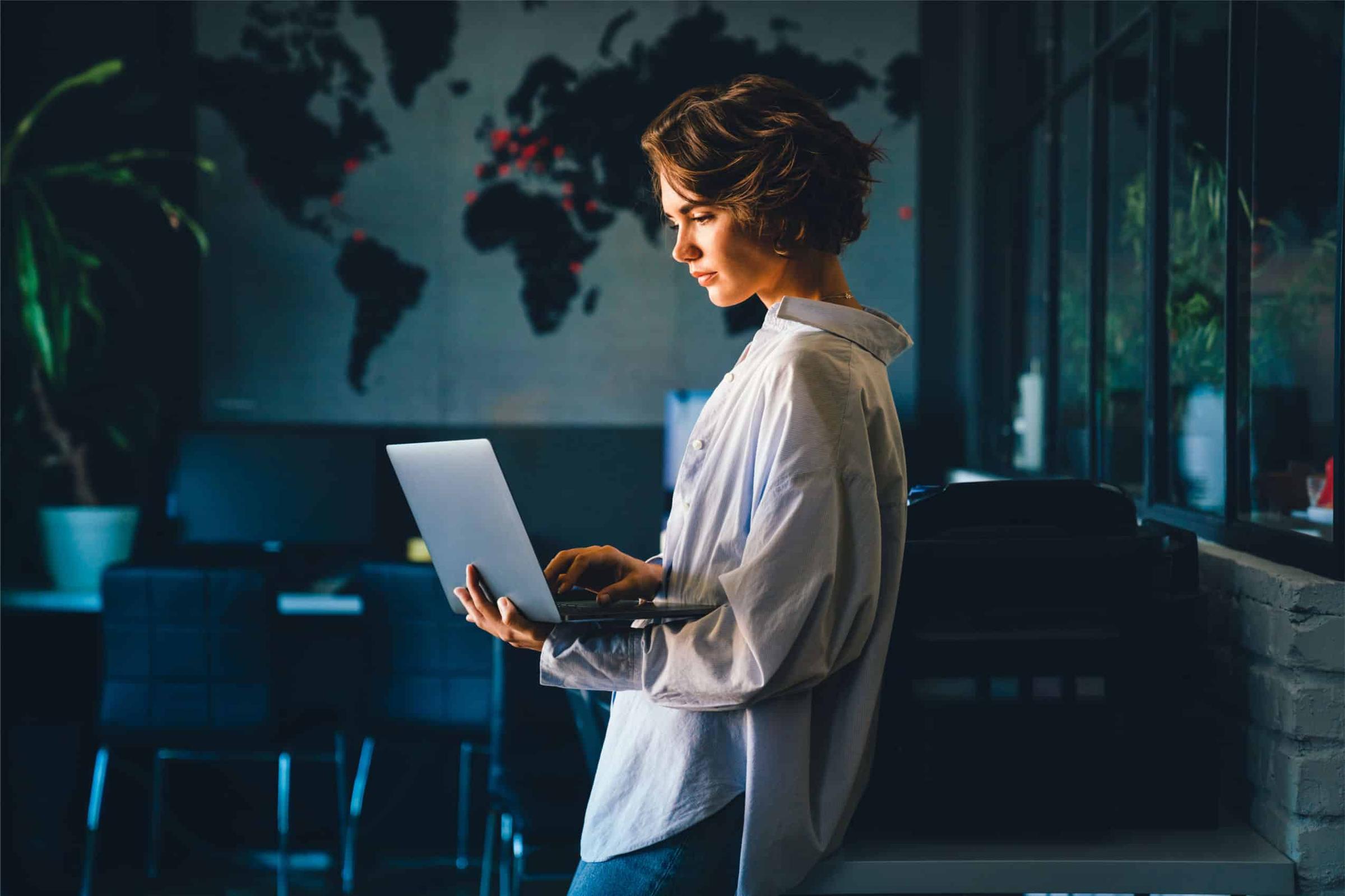 Woman working on a laptop in a dimly lit office with a world map on the wall