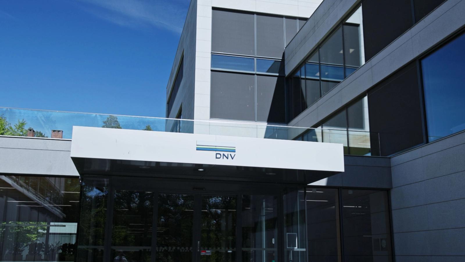 Das DNV-Logo auf dem Vordach über den gläsernen Eingangstüren eines modernen Bürogebäudes