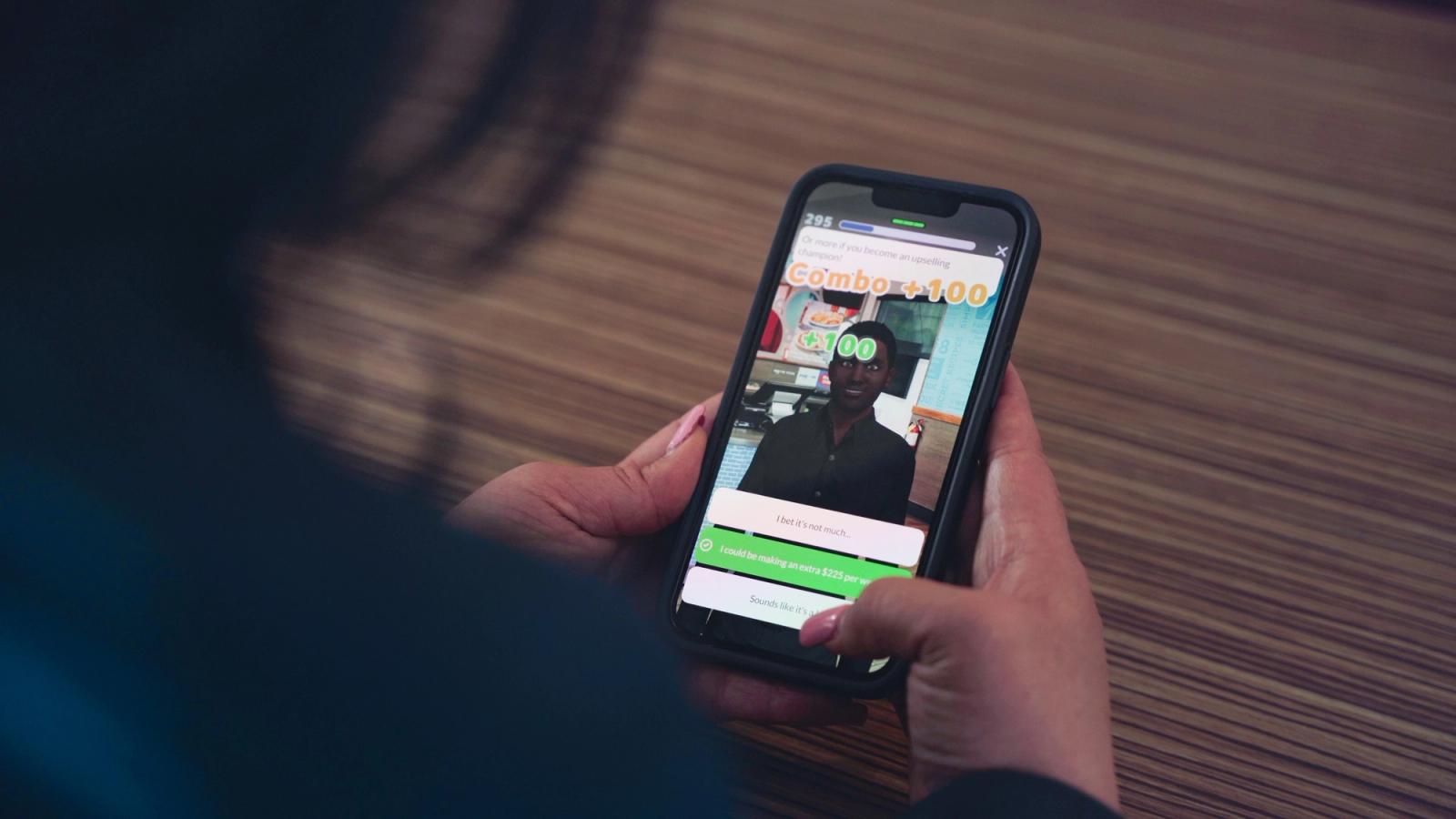 Blick über die Schulter auf ein Smartphone mit einem Trainingsspiel-Bildschirm und einem Combo-+100-Punkte-Popup