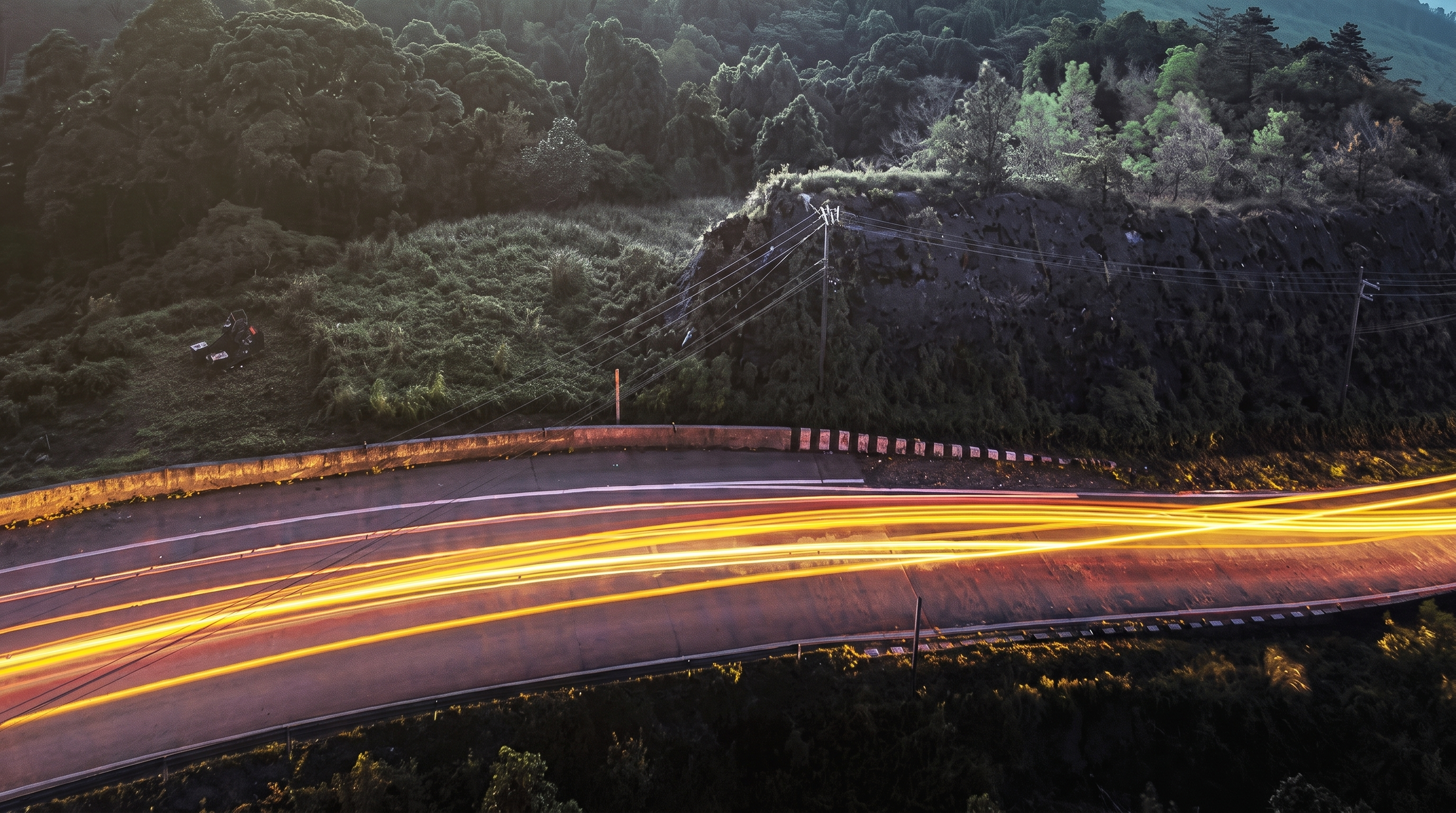 Long exposure photo of a winding road with light trails through a forested landscape.