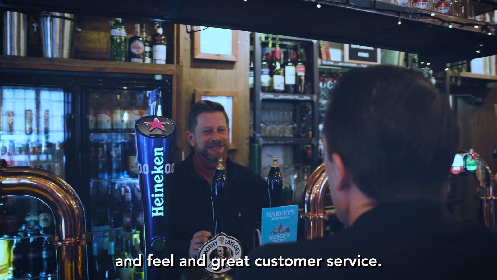 Ein lächelnder Barkeeper unterhält sich mit einem Gast an einer Pub-Theke mit aufgereihten Zapfhähnen