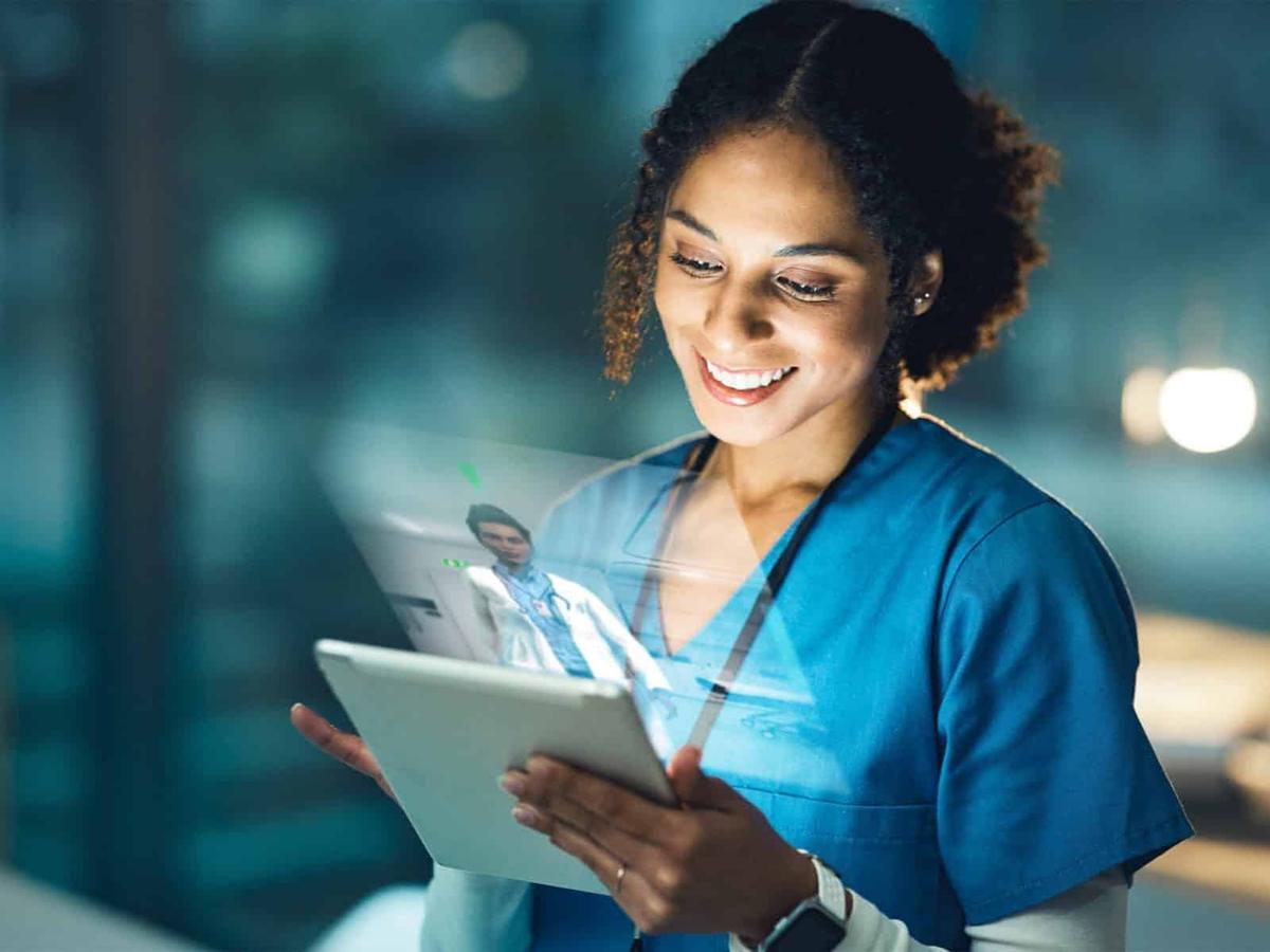 A smiling healthcare professional uses a tablet for a virtual consultation.