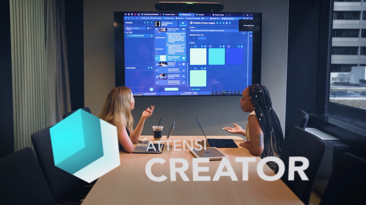 Two women at a meeting room table working in Attensi Creator on a large wall screen