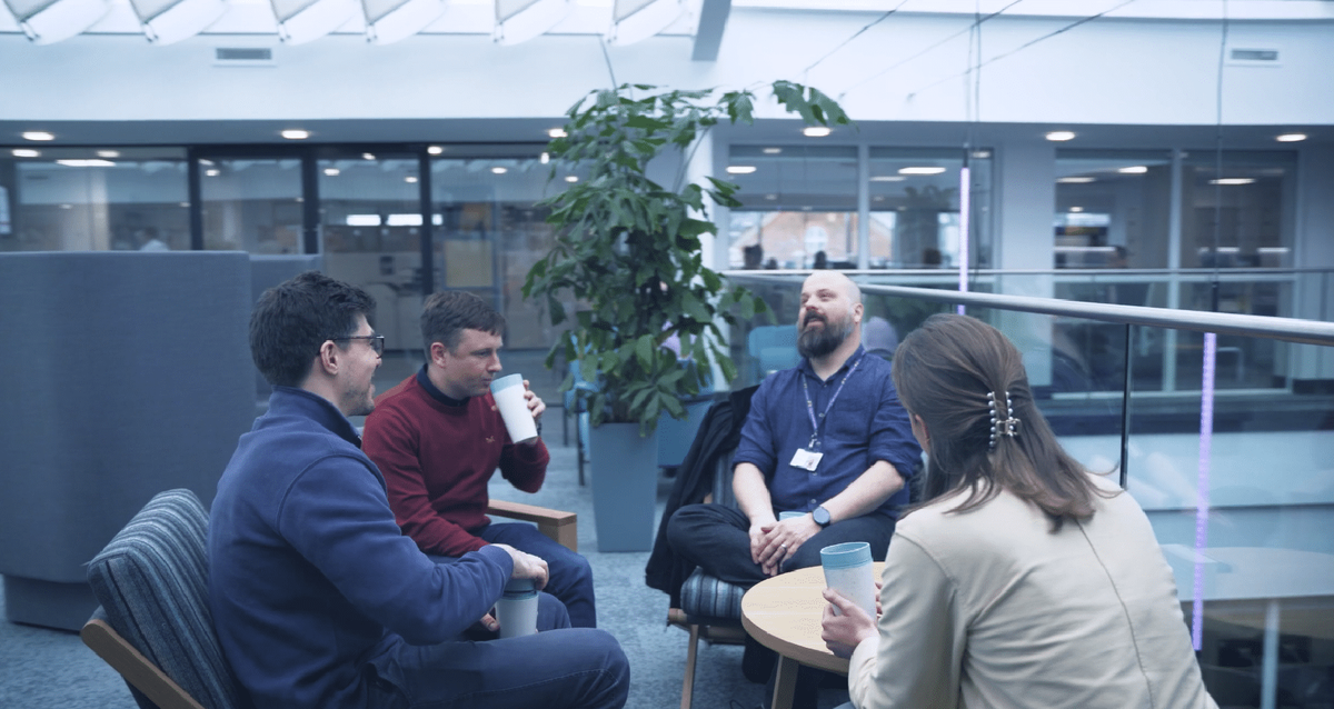 Vier Kolleginnen und Kollegen der Leeds Building Society unterhalten sich bei einem Kaffee in einem hellen Büroatrium