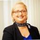 Alma Hannesdóttir lächelt im Porträt, mit Brille, schwarzem Blazer und gemustertem Schal