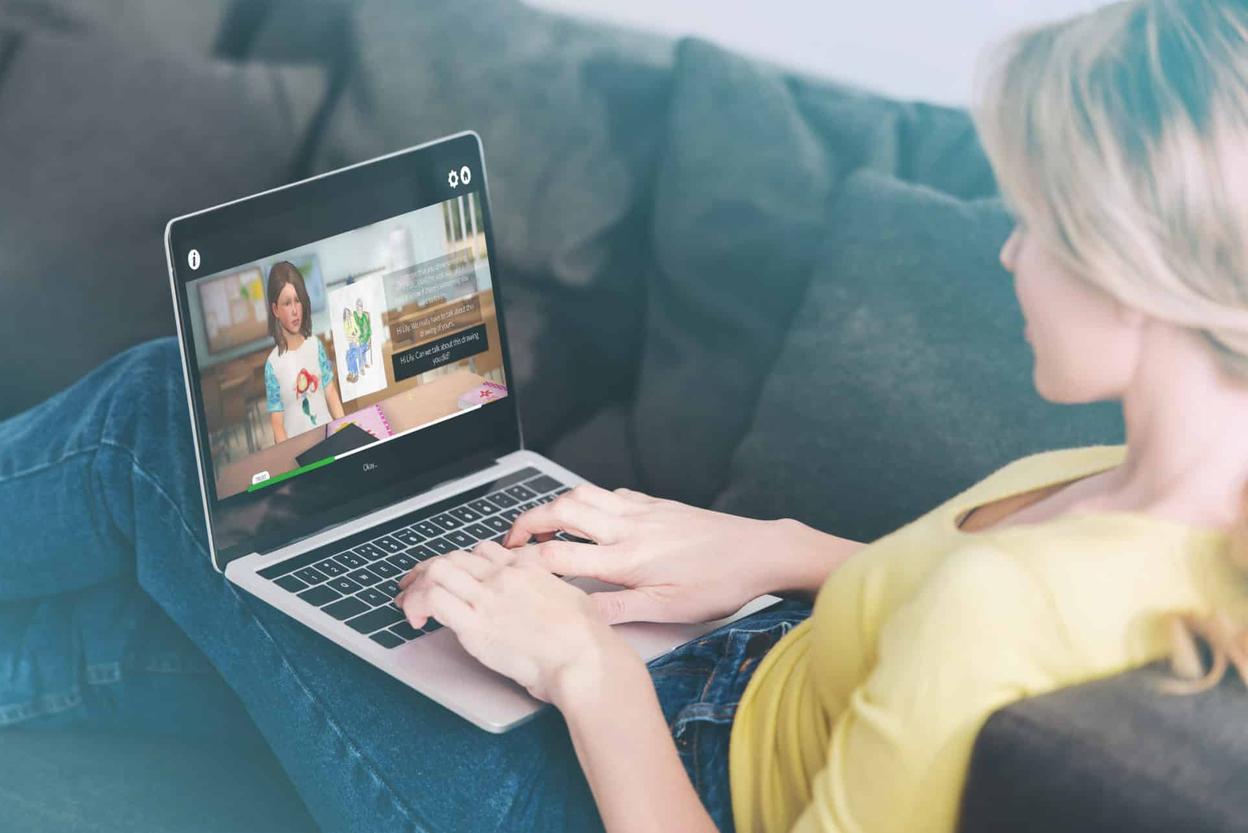 Frau auf einem Sofa nutzt einen Laptop mit der Simulation „Talk to Me“ und einer animierten Kinderfigur