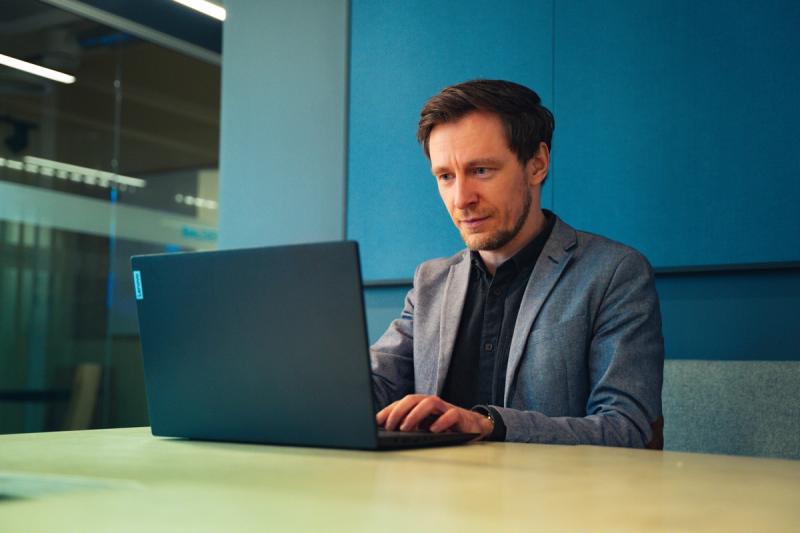 Mann in grauem Blazer arbeitet an einem Laptop in einem Besprechungsraum mit blauen Wänden