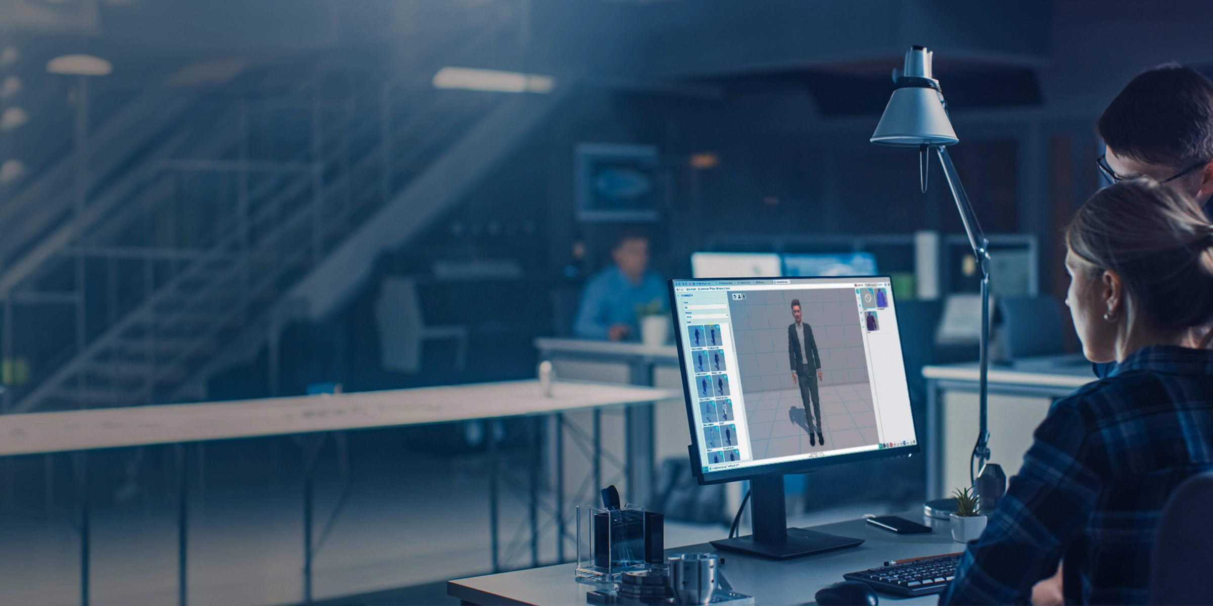 Zwei Kollegen am Schreibtisch bearbeiten einen 3D-Avatar auf einem Monitor in einem dunklen Büro