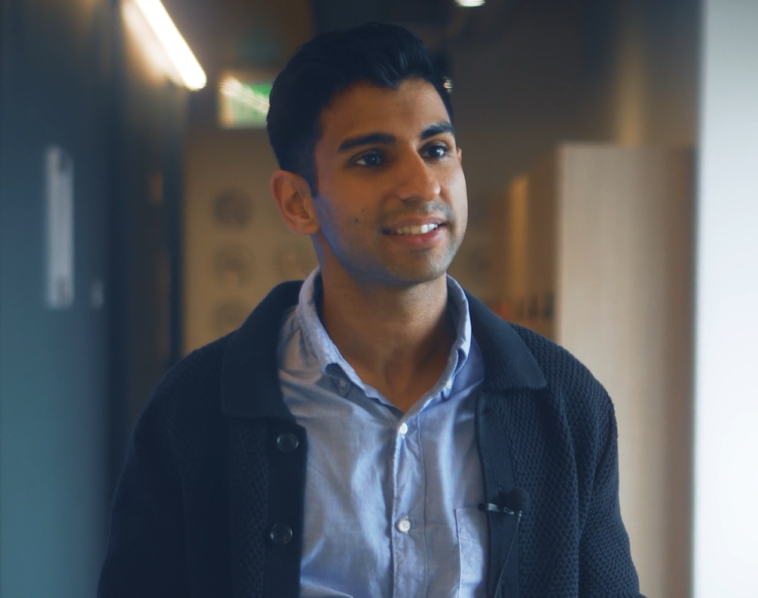 Varun Amesur, ein lächelnder junger Mann in dunkler Strickjacke und blauem Hemd