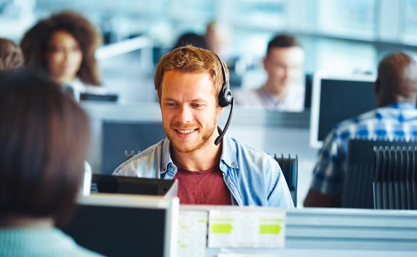 Callcenter-Mitarbeitende mit Headsets an Schreibtischen in einem Großraumbüro