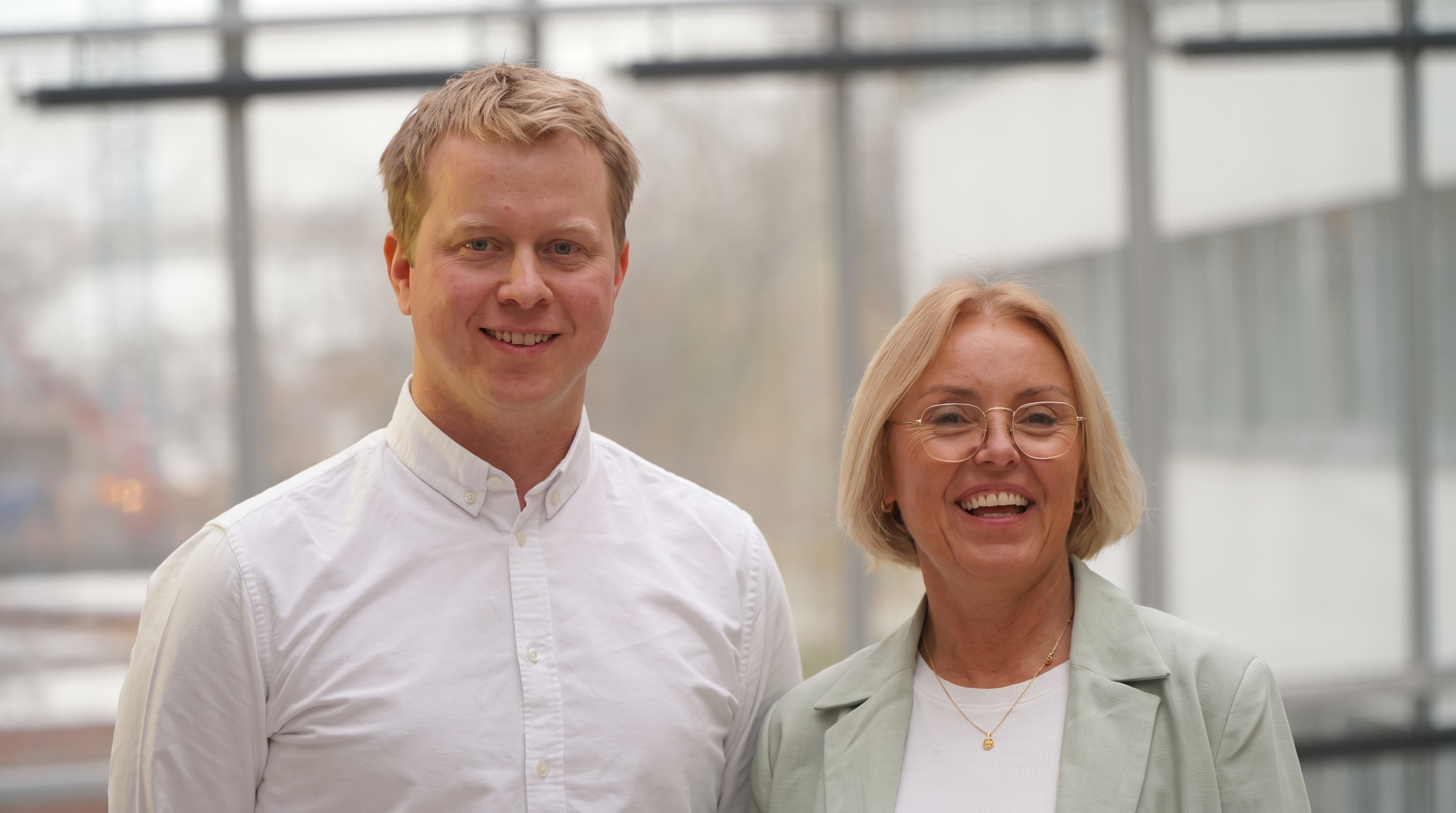 A man in a white shirt and a woman in a light green blazer smiling.