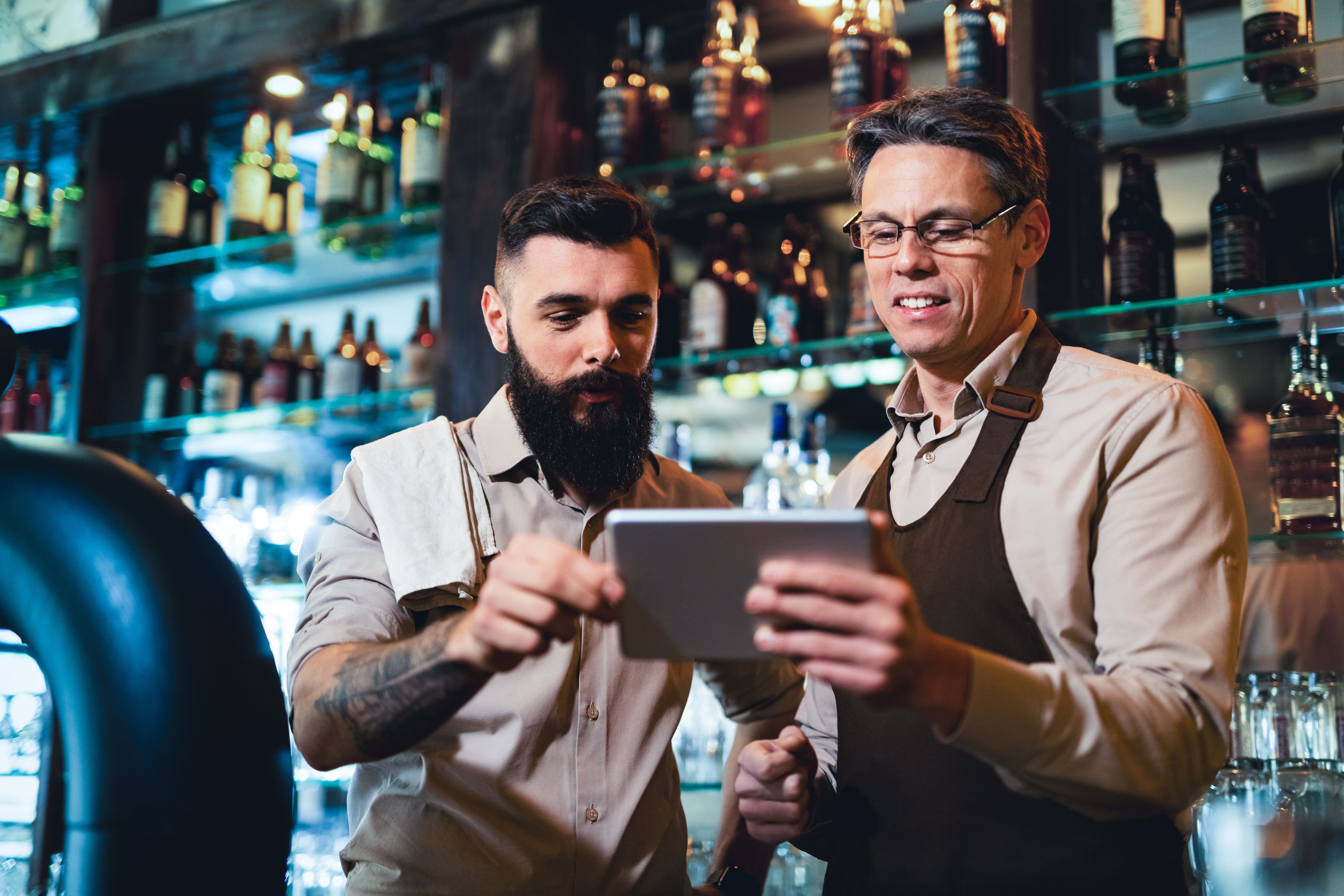 Two bartenders looking at a tablet behind a bar.