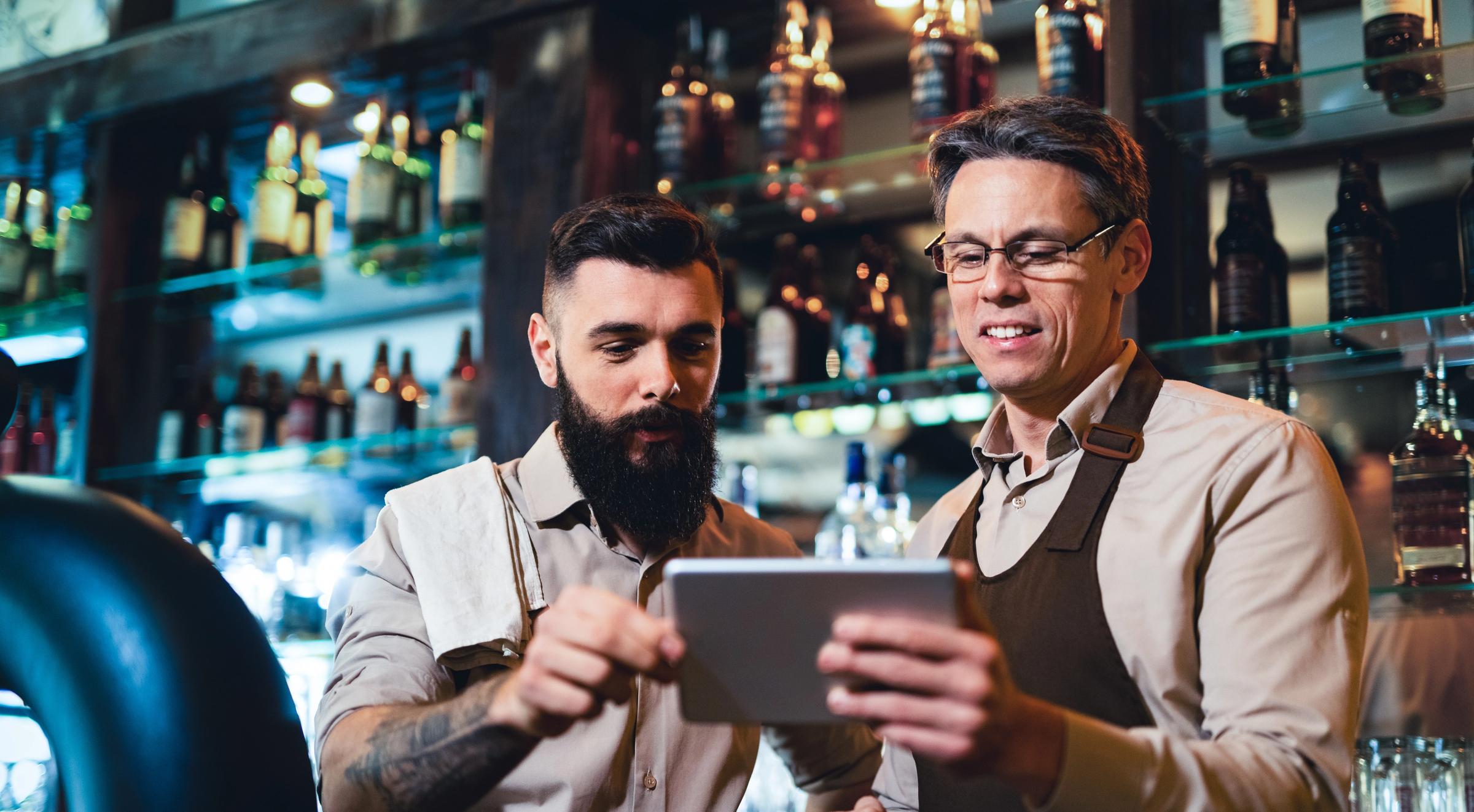 Two bartenders looking at a tablet behind a bar.