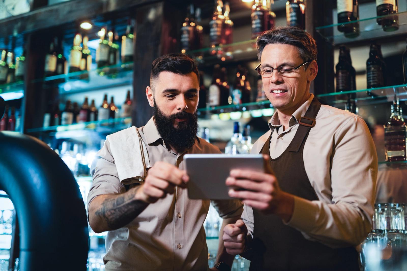 Two bar staff in aprons looking at a tablet together behind the bar