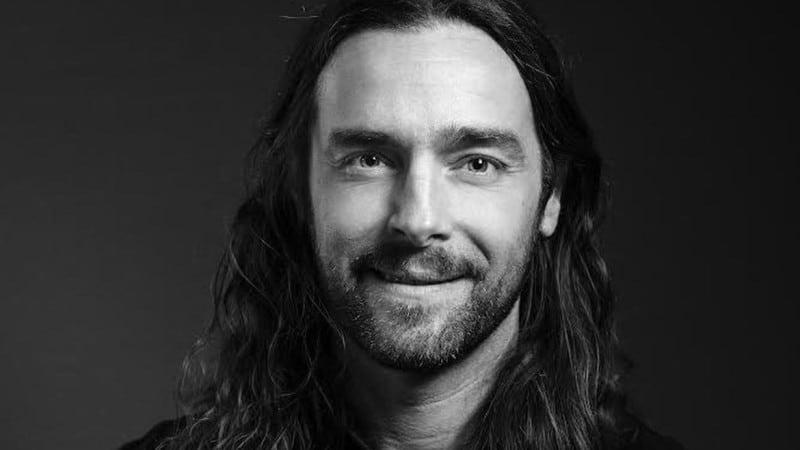 Marcus Wärn smiling in a black-and-white portrait, with long hair and a short beard