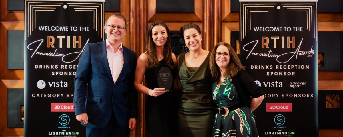 Four people with a glass trophy standing between two RTIH Innovation Awards sponsor banners