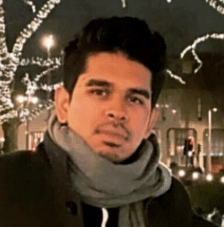 Abid Hussain outdoors at night, wearing a scarf among strings of fairy lights