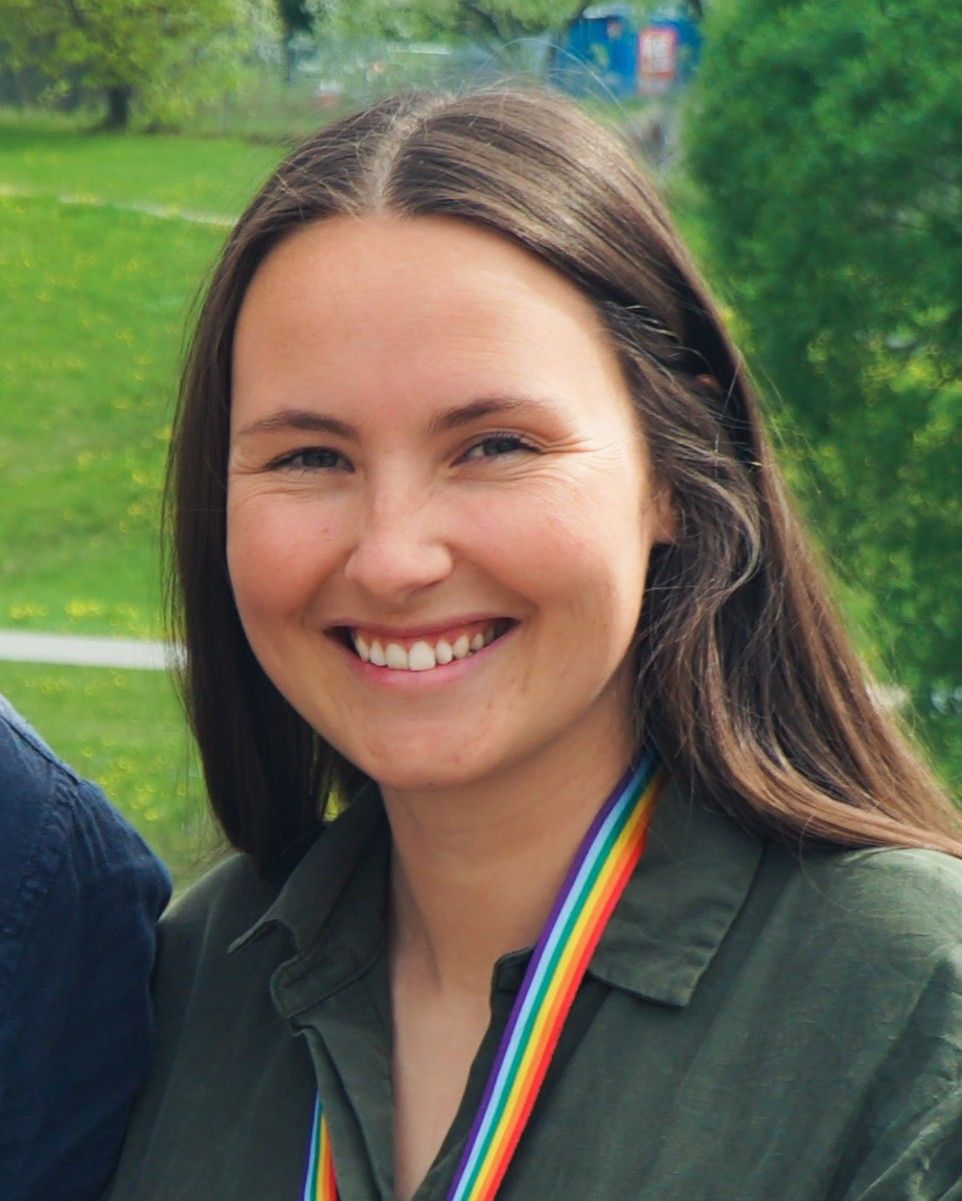 Tuva Lønne smiles outdoors, wearing an olive shirt and a rainbow lanyard