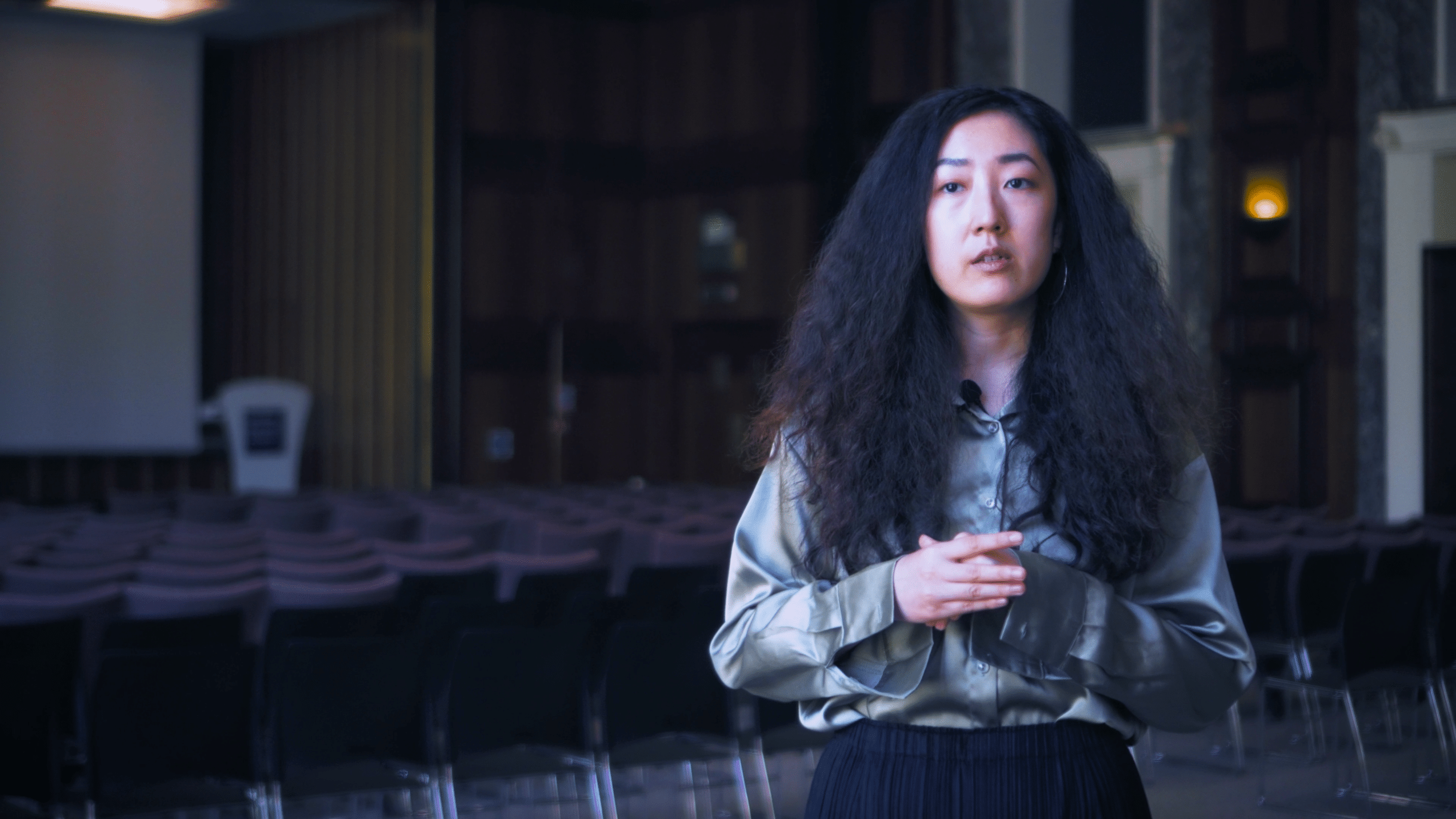 Ziyi, eine Frau in einer Satinbluse, spricht in einem leeren Hörsaal