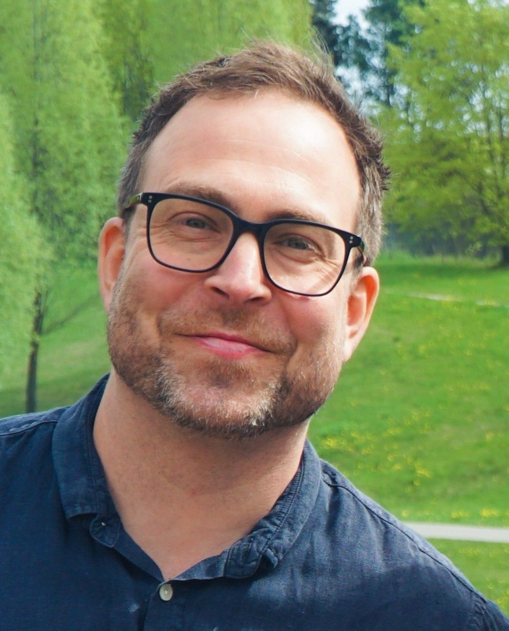 Dan Bjørke smiles outdoors, wearing glasses and a dark blue shirt