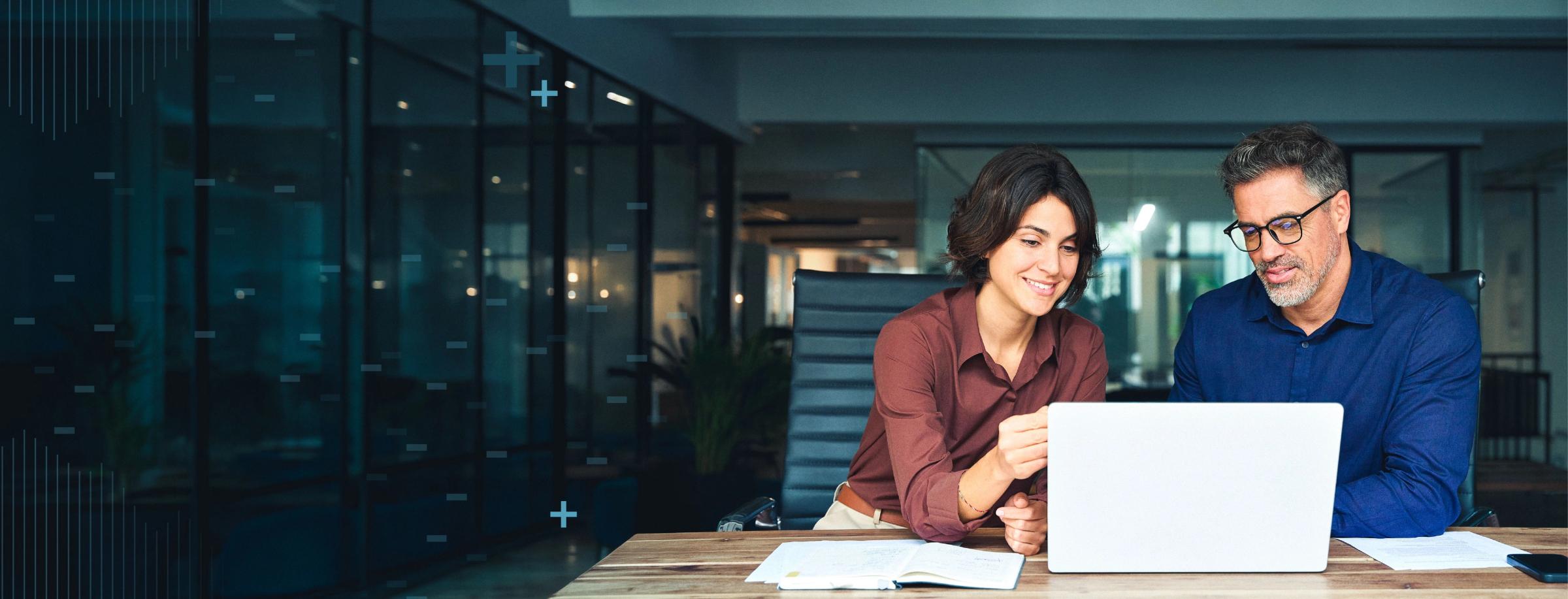 A man and a woman smiling while looking at a laptop in a modern office.